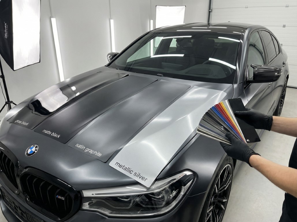 Образцы виниловой пленки на капоте автомобиля, в руках человека, который держит веер над капотом