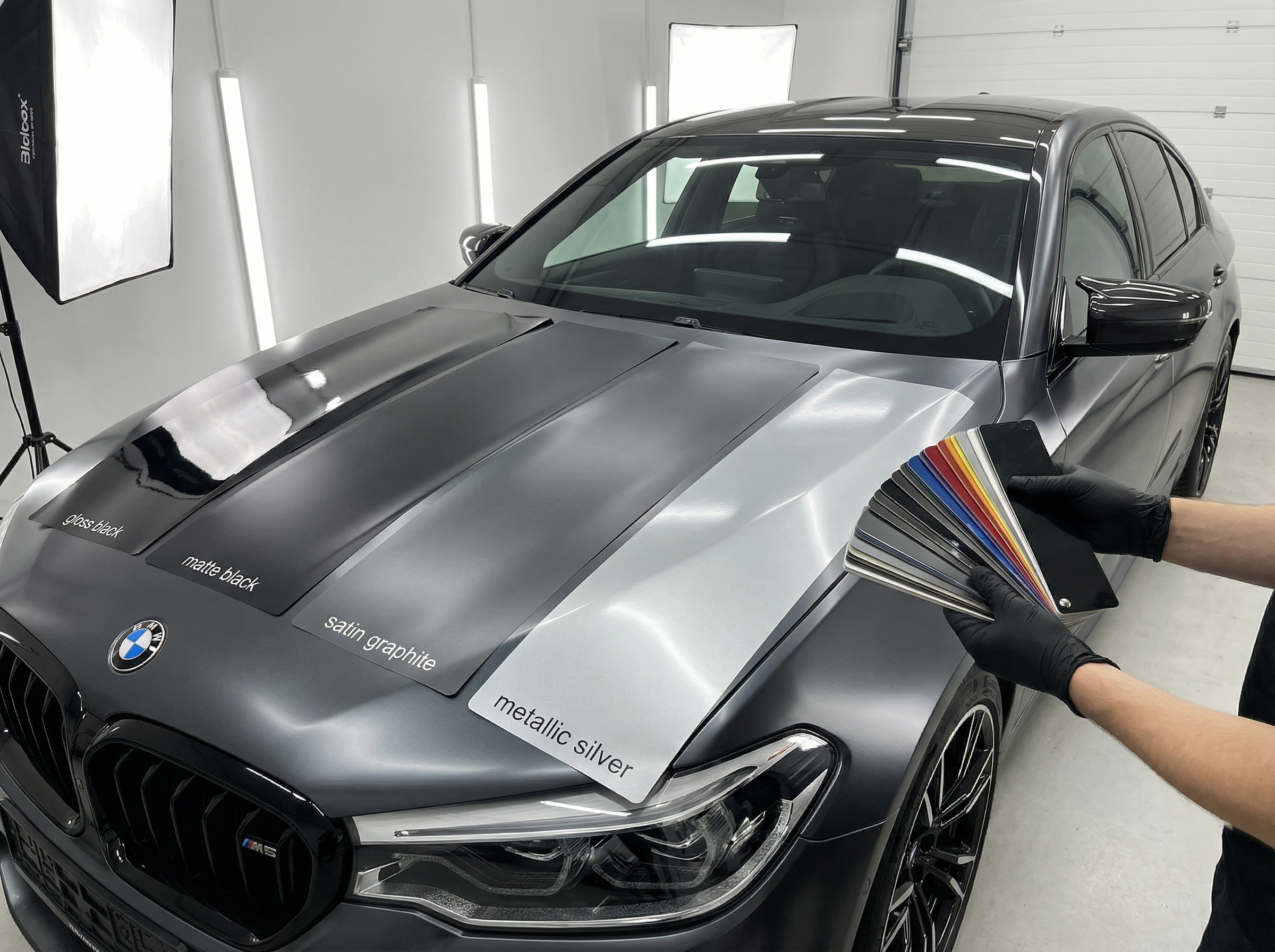 Образцы виниловой пленки на капоте автомобиля, в руках человека, который держит веер над капотом